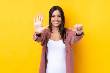 Genç esmer kadın izole edilmiş sarı arka planda altı parmaklı sayıyor.