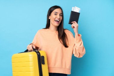 Genç esmer kadın izole edilmiş mavi arka planda tatilde bavul ve pasaportla