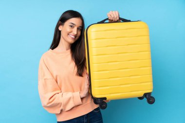 Genç esmer kadın izole edilmiş mavi arka planda seyahat valiziyle tatilde.