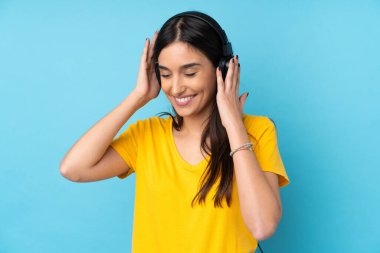 Genç esmer kadın izole edilmiş mavi arka planda müzik dinliyor.