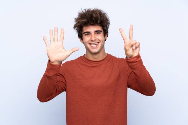 İzole edilmiş mavi arka plan üzerinde genç beyaz adam parmaklarıyla yediyi sayıyor