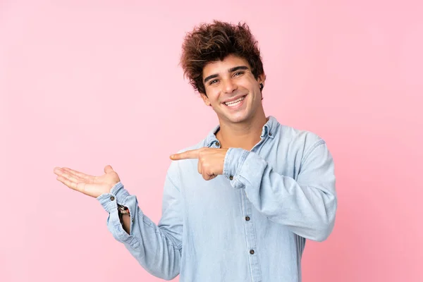 若いですCaucasian男とともにJeanシャツ上の隔離されたピンクの背景保持コピースペース想像上のザ手のひらに挿入する広告 — ストック写真