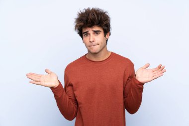 İzole edilmiş mavi arka planda genç beyaz adam ellerini kaldırırken şüpheye düşüyor.