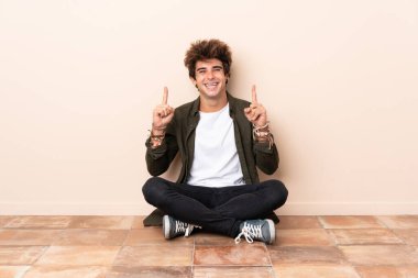 Genç, beyaz bir adam yerde oturmuş harika bir fikri işaret ediyor.