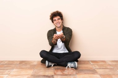 Kafkasyalı genç bir adam yerde oturuyor ve bir ilan vermek için fotokopi makinesini avucunun içinde tutuyor.