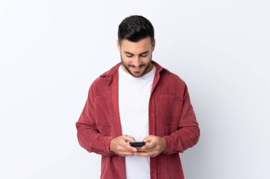 Sakallı, kadife ceket giyen genç yakışıklı bir adam izole edilmiş beyaz arka planda cep telefonuyla bir mesaj gönderiyor.