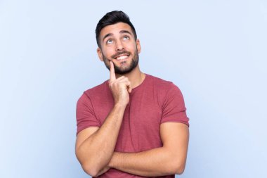 Mavi arka planda sakallı yakışıklı genç adam yukarı bakarken bir fikir düşünüyor.