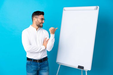 İş adamı beyaz tahtada sunum yapıyor. Beyaz tahtada sunum yapıyor ve yan tarafı işaret ediyor.