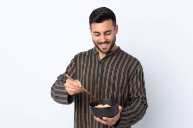 Arka planda izole edilmiş genç bir adam elinde yemek çubuklarıyla bir kase erişte tutuyor.