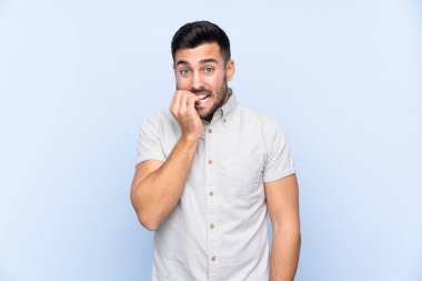 Sakallı, genç ve yakışıklı bir adam mavi arka planda gergin ve korkmuş.