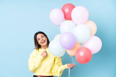 İzole edilmiş mavi arka planda balon tutan bir kadın zaferi kutluyor.