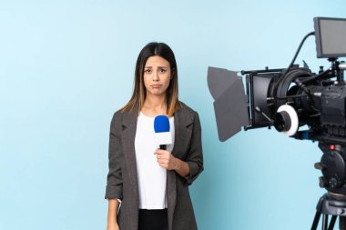 Muhabir kadın mikrofon tutuyor ve mavi arka planda üzücü haberler veriyor.