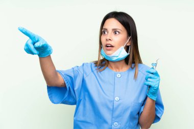 İzole edilmiş yeşil arka plan üzerinde araçları tutan kadın dişçi uzaklığı gösteriyor