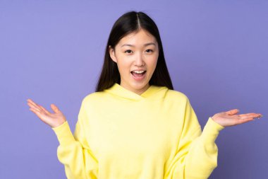 Genç Asyalı kadın mor arka planda izole edilmiş, şok olmuş yüz ifadesi var.