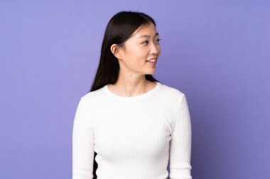 Mor arka planda izole edilmiş genç Asyalı kadın yana bakıyor ve gülümsüyor.