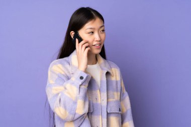 Mor arka planda izole edilmiş genç Asyalı bir kadın cep telefonuyla sohbet ediyor.