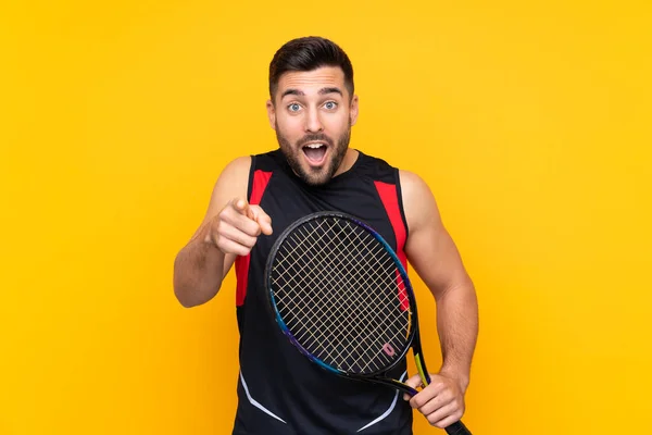 テニスプレーヤー男上の隔離された黄色の壁驚きと指摘フロント — ストック写真