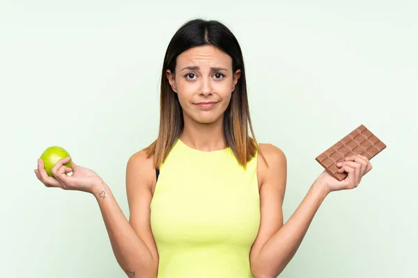 Žena Nad Izolovaným Zeleným Pozadím Pochybnostmi Při Užívání Čokoládové Tablety — Stock fotografie