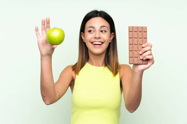 Žena Izolovaném Zeleném Pozadí Čokoládovou Tabletou Jedné Ruce Jablkem Druhé — Stock fotografie