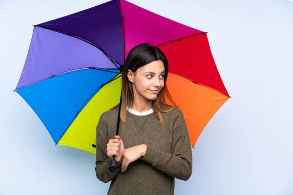 Joven Morena Sosteniendo Paraguas Sobre Una Pared Azul Aislada Pensando — Foto de Stock