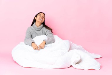 Genç melez kadın pijama giymiş yerde oturmuş gülüyor.