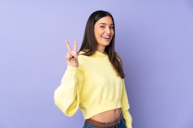 İzole edilmiş arka planda gülümseyen ve zafer işareti gösteren beyaz bir kadın.