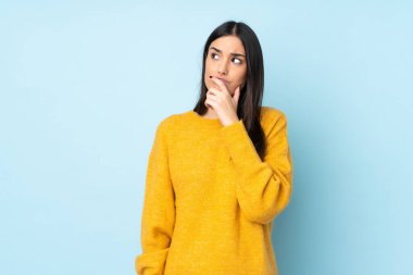 Kafkasyalı genç bir kadın mavi arka planda izole edilmiş. Şüpheleri var ve kafası karışmış bir yüz ifadesi var.