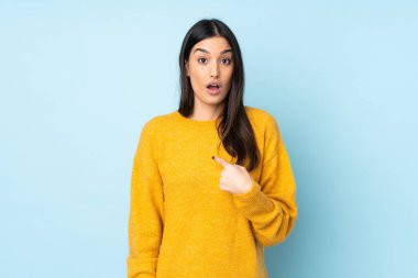 Mavi arka planda izole edilmiş genç beyaz kadın kendini işaret ediyor.