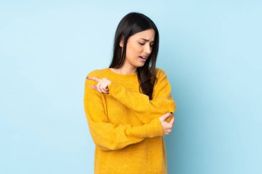 Genç beyaz kadın, mavi arka planda izole edilmiş, dirsek ağrısı var.