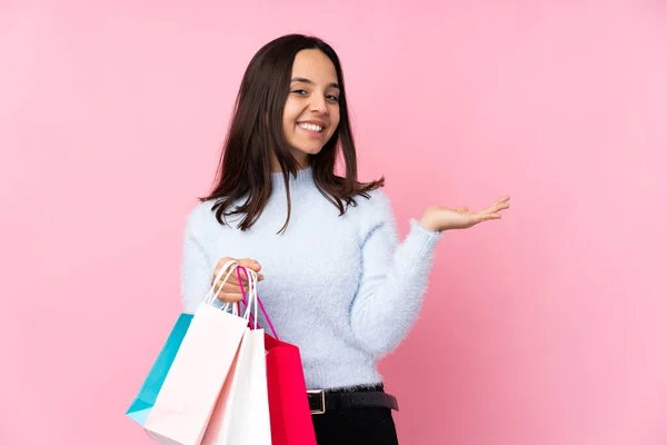 一个年轻的女人 提着购物袋在孤立的粉色背景上 手心拿着一个想象中的复制空间插入一个广告 — 图库照片