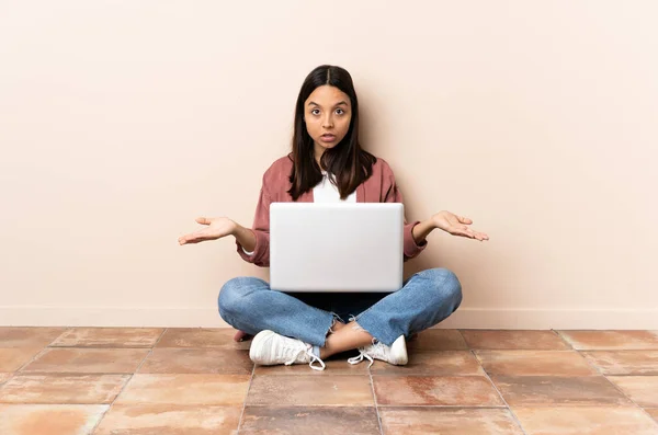 年轻的混血女子 手持笔记本电脑坐在地板上 摆出怀疑的姿势 — 图库照片