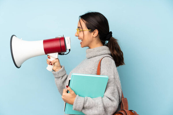 Young mixed race woman going to school isolated on blue background shouting through a megaphone