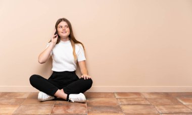 Ukraynalı genç kız yerde oturuyor cep telefonuyla sohbet ediyor.