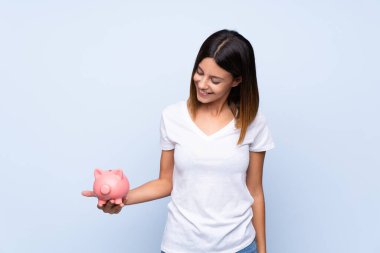 Soyutlanmış mavi arka planı olan genç bir kadın büyük bir kumbara tutuyor.