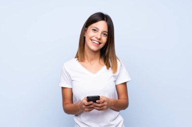 İzole edilmiş mavi arka plan üzerinde genç bir kadın cep telefonuyla bir mesaj ya da e-posta gönderiyor