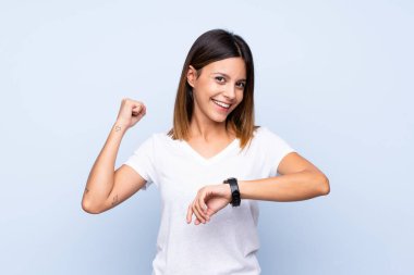 Kol saati ve şanslı ifadesiyle izole edilmiş mavi arka planı olan genç bir kadın.