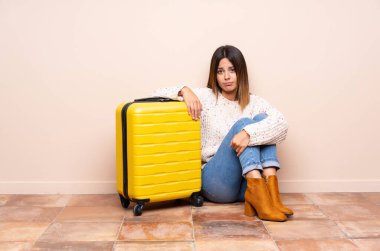 Bavullu gezgin kadın yerde oturuyor.