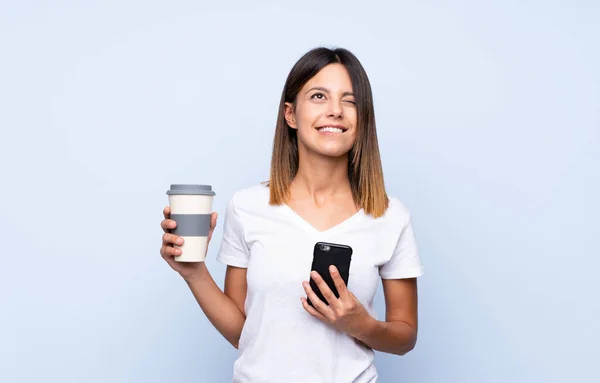 Giovane Donna Sfondo Blu Isolato Che Tiene Caffè Portare Cellulare — Foto Stock