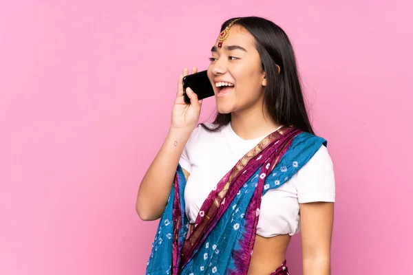 Young Indian woman with sari over isolated background keeping a conversation with the mobile phone