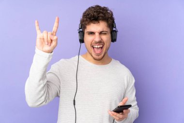 Mor arka planda izole edilmiş beyaz bir adam gezici bir rock hareketi yaparak müzik dinliyor.