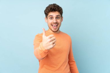 Beyaz adam mavi arka planda izole edildi. Başparmakları havada çünkü iyi bir şey oldu.