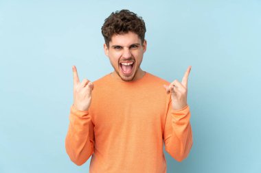 Beyaz adam mavi arka planda izole edilmiş kaya jestleri yapıyor.