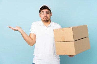 Teslimatçı beyaz adam mavi arka planda izole edilmiş, kafası karışmış yüz ifadesi ile ilgili şüpheleri var.