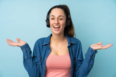 Genç esmer kadın soyutlanmış mavi arka planda şaşırmış ve müzik dinliyor.