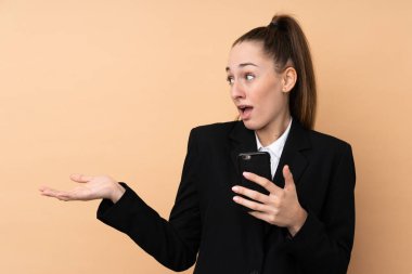 Genç bir iş kadını, izole edilmiş arka planda cep telefonu kullanıyor. Sürpriz yüz ifadesi var.