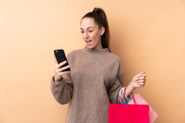 Genç esmer kadın, izole edilmiş arka planda alışveriş torbaları tutuyor ve bir arkadaşına cep telefonuyla bir mesaj yazıyor.