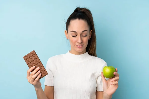 Young Brunette Woman Isolated Blue Background Taking Chocolate Tablet One — Stock Photo, Image