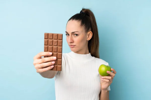 Young Brunette Woman Isolated Blue Background Taking Chocolate Tablet One — 스톡 사진