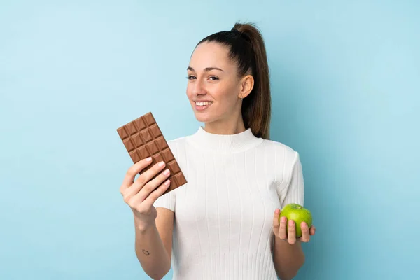 Young Brunette Woman Isolated Blue Background Taking Chocolate Tablet One — 스톡 사진