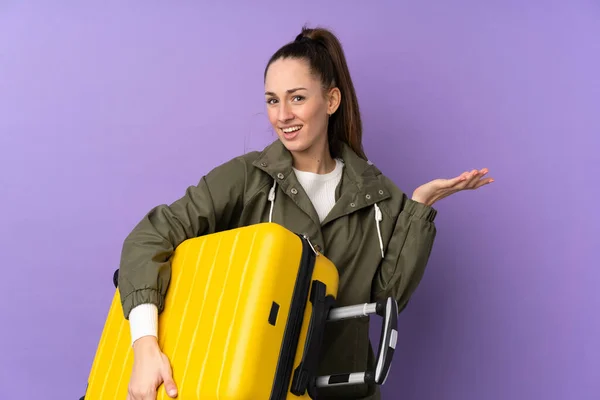 年轻的黑发女人带着旅行箱在孤立的紫色背景上度假 — 图库照片